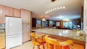 Eine Küche mit Holzausstattung, einem weißen Kühlschrank, einer Granitarbeitsplatte und Holzbarhocker.