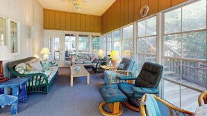 Ein großzügiger Raum mit einem großen Fenster, einem Deckenventilator und verschiedenen Sitzgelegenheiten, darunter eine Couch, Stühle und ein kleiner Tisch.