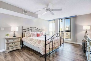Un dormitorio con cama, mesitas de noche, ventilador de techo y ventana con persianas.