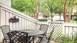 Eine Terrasse mit einem runden Metalltisch und vier Stühlen, einem Willkommensschild und einem weißen Ziergartenzaun.