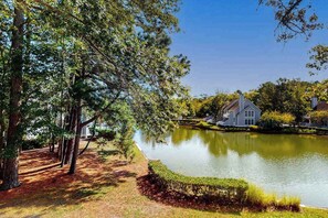 A serene lakeside property with a house, trees, and a well-maintained lawn. - Sea Colony Tennis 2nd floor condo w/ basketball court, shared sauna, and pool (Bethany Beach)