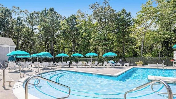 Una piscina con lettini e ombrelloni, circondata da alberi.