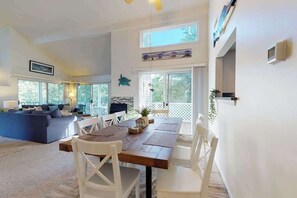 A spacious living area with a dining table, white chairs, a blue sofa, and large windows. - Sea Colony Tennis 2nd floor condo w/ gym, basketball court, and lake view (Bethany Beach)