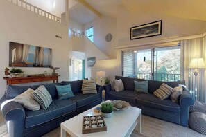 A spacious living room with two dark blue sofas, a white coffee table, and a staircase leading to an upper level. - Sea Colony Tennis 2nd floor condo w/ gym, basketball court, and lake view (Bethany Beach)