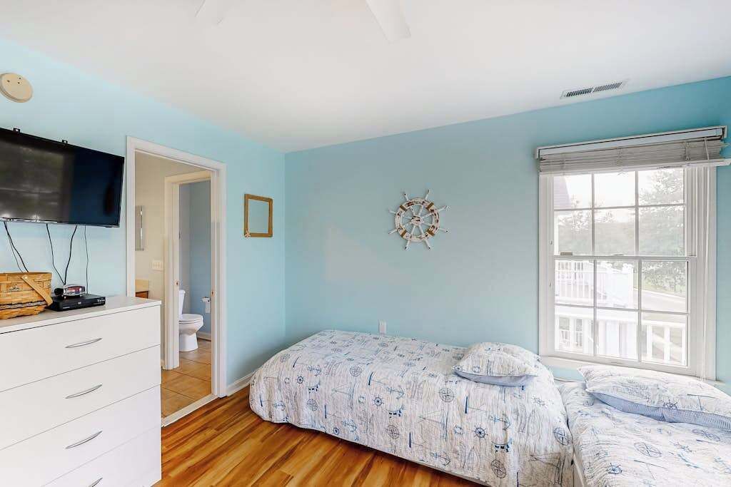 Une chambre à coucher comprenant un lit, une commode, un téléviseur, une fenêtre et une porte donnant sur une salle de bain.