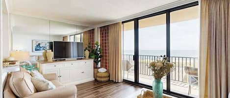 Ein modernes Wohnzimmer mit einer Couch, einem Fernseher und großen Fenstern mit Blick auf einen Balkon.