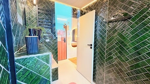 Un baño moderno con puerta de cristal, una planta en maceta y un espejo.