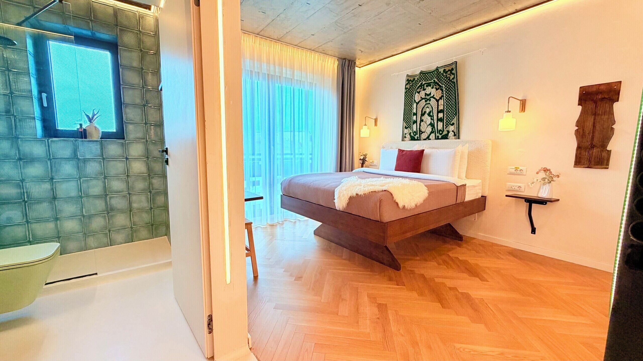 Un dormitorio moderno con cama, mesitas de noche, una ventana con cortinas y un baño con puerta de cristal.