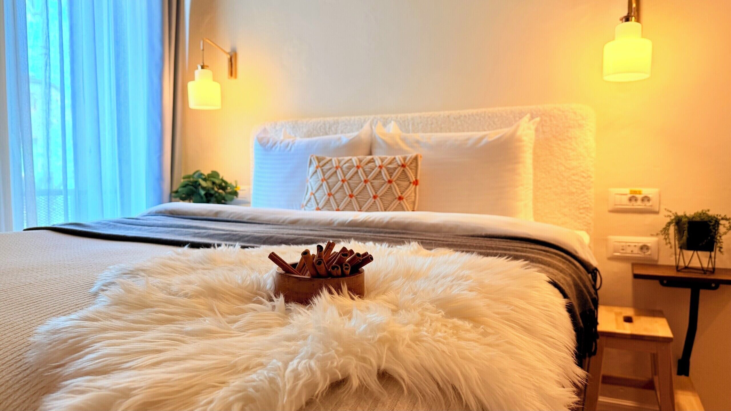 A bedroom with a bed, fluffy white rug, a small wooden side table, and wall-mounted lamps.