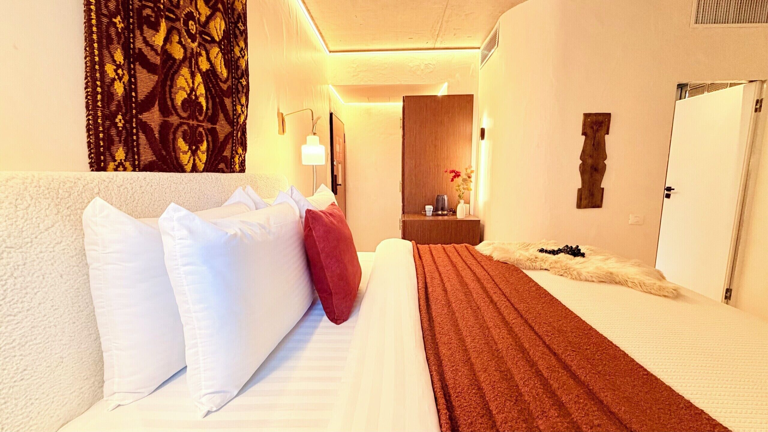 Una habitación de hotel con cama, mesita de noche, espejo y puerta.
