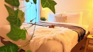 Un letto rifatto con cura, con una soffice coperta bianca, un cuscino decorato e un comodino con una lampada.