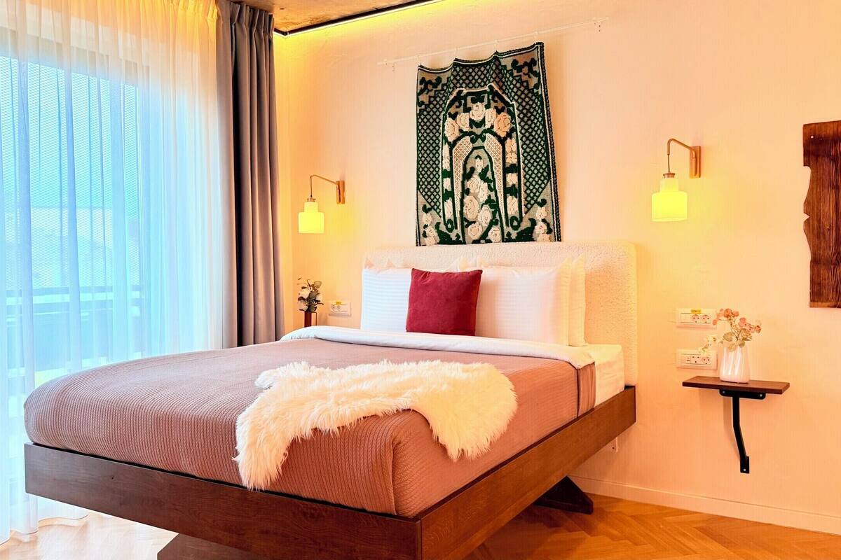 A modern bedroom with a bed, a nightstand, a wall tapestry, and a window with curtains.