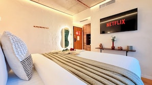 A modern hotel room with a bed, a wall-mounted TV, a wooden cabinet, and a mirror. - Modern Studios Steps from Piața Romană (Bucharest)