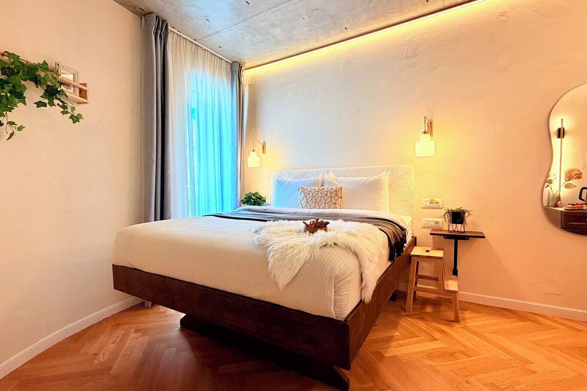 A modern bedroom with a bed, bedside table, and a mirror.