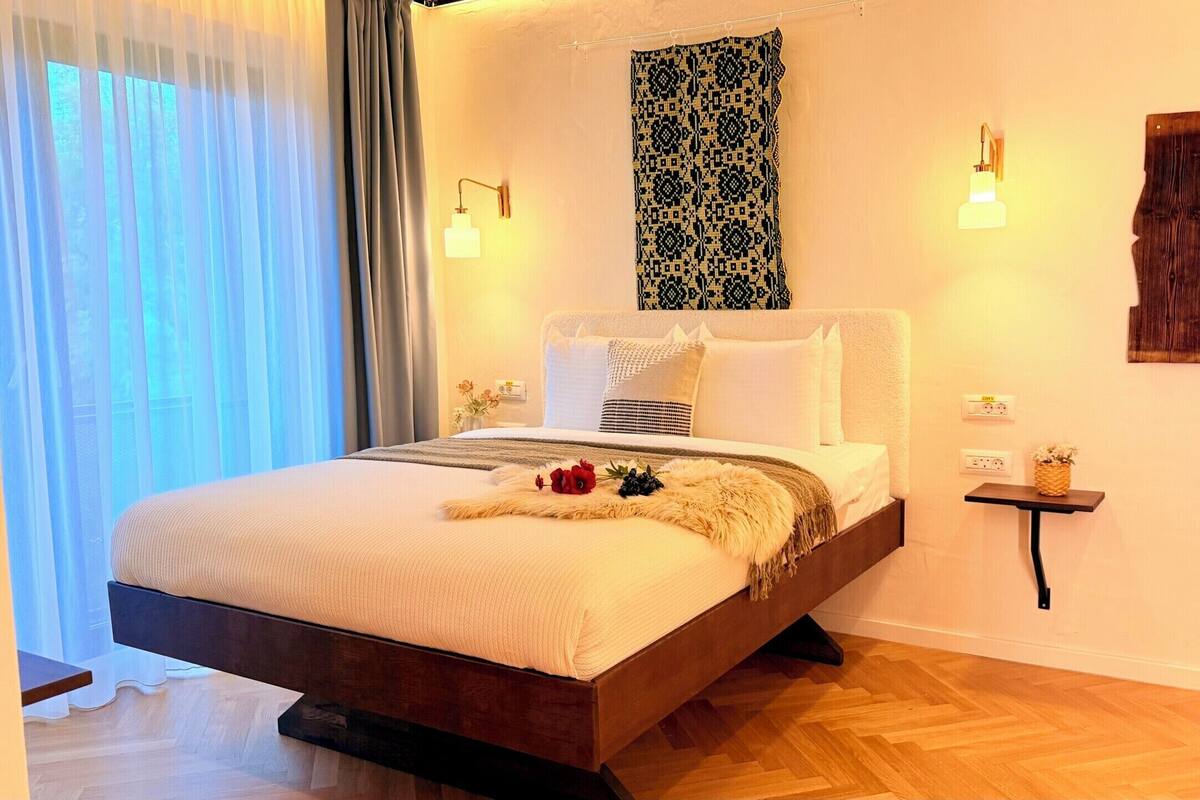 A bedroom with a bed, bedside tables, a wall-mounted light, and a patterned tapestry.