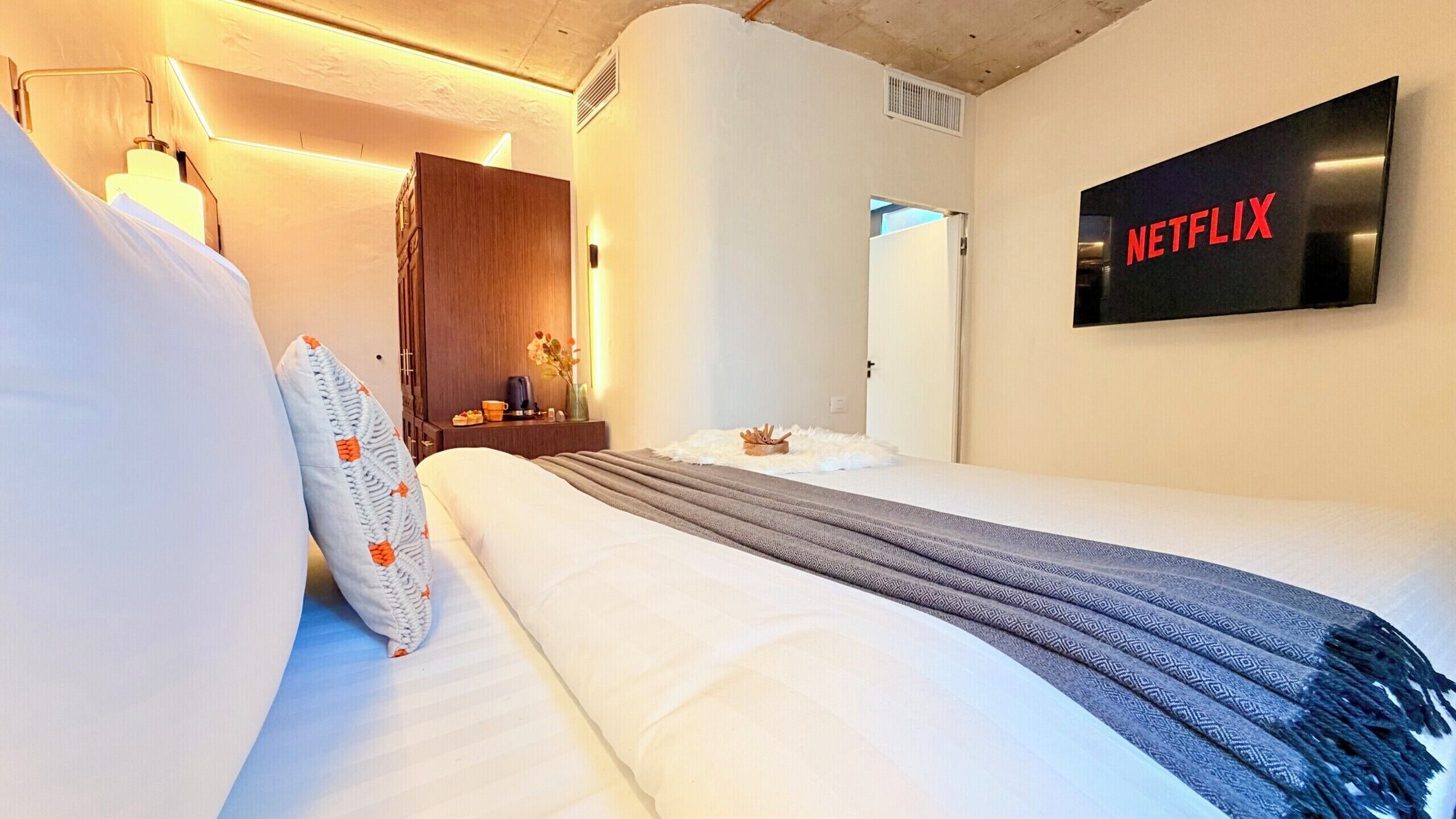 Una habitación de hotel con una cama, un televisor montado en la pared y un armario de madera.