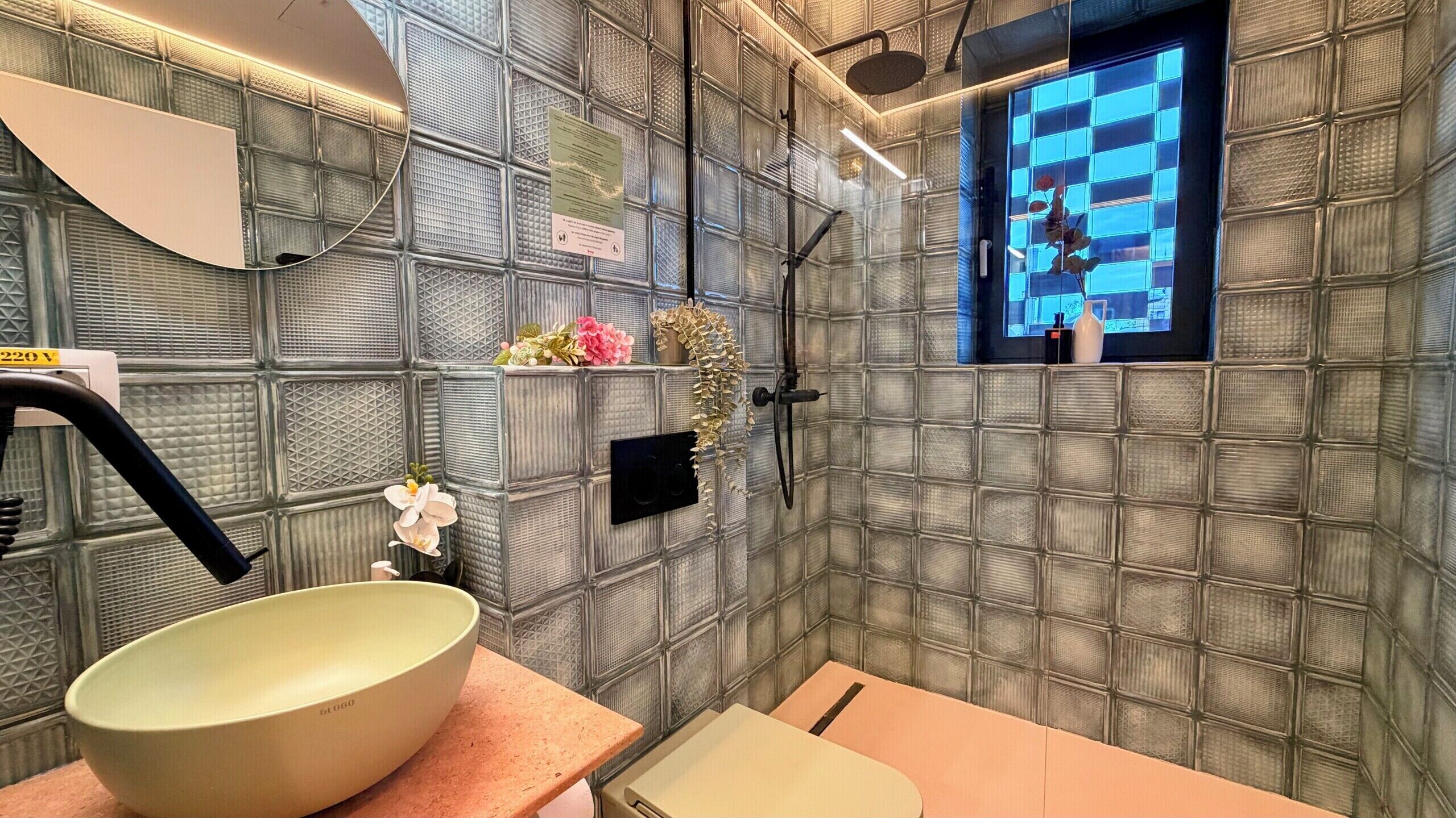 A bathroom with a large bowl sink, a shower, and a window with a view.