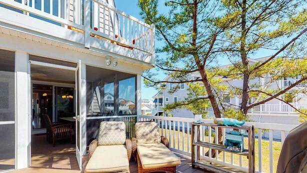 Un balcón con mobiliario de mimbre, baranda blanca y vistas a casas y árboles.