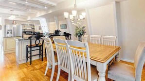 Una cocina moderna con comedor, mesa de madera, sillas blancas y una araña.