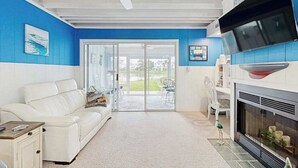 A living room with a white sofa, a fireplace, a ceiling fan, and a large window.
