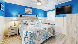 A bedroom with a bed, nightstands, a ceiling fan, a TV, and a window with blinds.