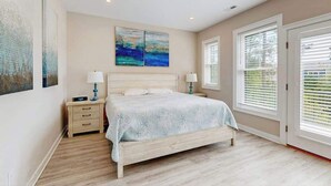 Une chambre à coucher comprenant un lit, des tables de chevet, une commode, une fenêtre avec des stores et des œuvres d’art accrochées aux murs.