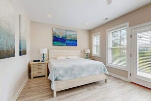 A bedroom with a bed, bedside tables, a nightstand, a window with blinds, and artwork on the walls. - Pond Acres paradise with sunroom, central AC, & washer/dryer (Bethany Beach)