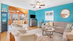 A living room with a blue wall, wooden ceiling, a ceiling fan, a television, a sofa, a coffee table, and a dining area in the background. - Town of Bethany Beach Home Near Fun Activities & Adventures w/Free WiFi & WD (Bethany Beach)