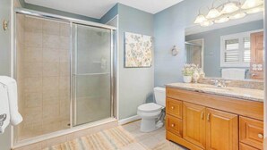A bathroom with a glass shower enclosure, a toilet, wooden cabinets, and a mirror with lights. - Town of Bethany Beach Home Near Fun Activities & Adventures w/Free WiFi & WD (Bethany Beach)