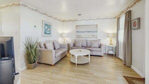 Ein Wohnzimmer mit zwei Sofas, einem Couchtisch, einem Fernseher und einem Bild an der Wand.