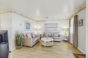 A living room with two sofas, a coffee table, a TV, and a painting on the wall. - Fenwick Island Condo on 2nd Floor w/Free WiFi, Washer/Dryer, Central AC, & Cable (Fenwick Island)