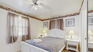 Ein Schlafzimmer mit einem Bett, Nachttischen, einem Deckenventilator und Vorhängen.
