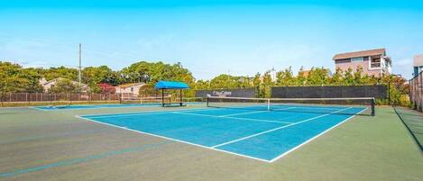 A tennis court with a net, surrounded by a fence, and a building in the background.