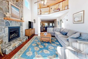 A living room with a stone fireplace, a sofa, a coffee table, and a staircase leading to an upper level. - Town of Bethany Beach oceanfront home with pool & tennis access, washer/dryer (Bethany Beach)