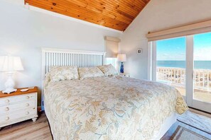 A bedroom with a bed, a nightstand, a lamp, a window with a view of the beach, and a wooden ceiling. - Town of Bethany Beach oceanfront home with pool & tennis access, washer/dryer (Bethany Beach)