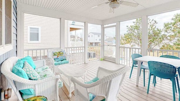 Eine überdachte Terrasse im Freien mit Rattanmöbeln, einem Deckenventilator und großen Fenstern.