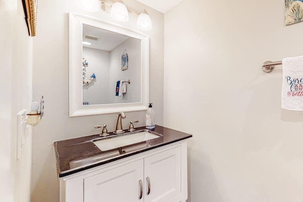 A bathroom with a white vanity, a sink, a mirror, and a towel rack.