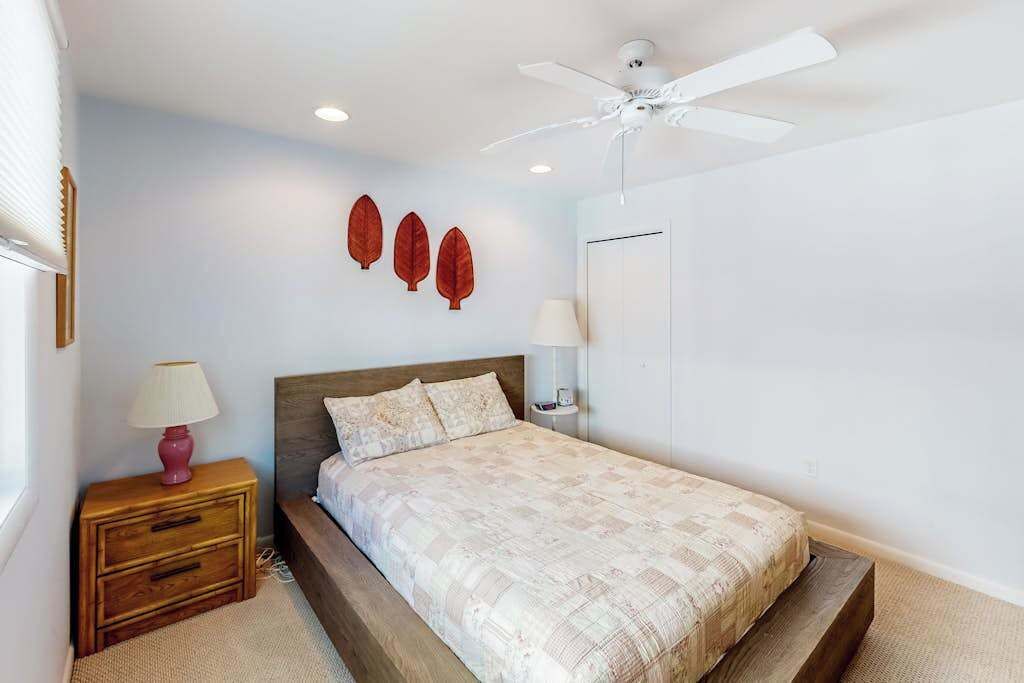 Un dormitorio con cama, mesitas de noche, ventilador de techo y lámparas fijadas a la pared.