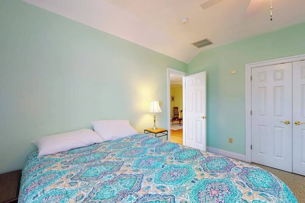 A bedroom with a bed, a nightstand, a lamp, and a door leading to another room.