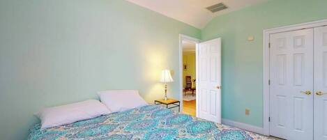 A bedroom with a bed, a nightstand, a lamp, and a door leading to another room.