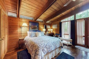 Ein Schlafzimmer in einer Blockhütte mit einem Bett, Nachttischlampen, einer Bank und einem großen Fenster.