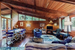 Ein Holzblockbau-Innenraum mit Esstisch, blauen Stühlen, einer Couch, einem Glastisch und einem Kamin.