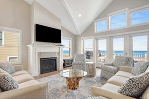 Un salón espacioso con chimenea, un televisor de pantalla plana montado encima y un balcón con vistas al océano.