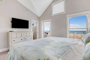 Un dormitorio con cama, cómoda, televisor y balcón con vista a la playa.