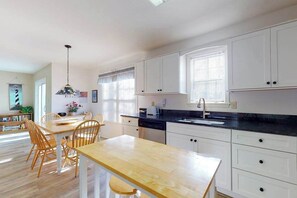 A kitchen with white cabinets, a wooden dining table, and a black countertop. - Cottages on Whites Creek house near beach w/private W/D, shared pool, free WiFi (Ocean View)