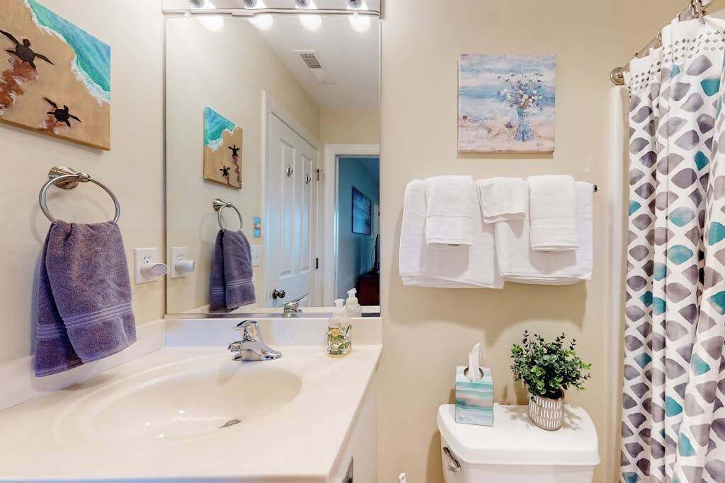 A bathroom with a sink, mirror, towels, and a shower curtain.