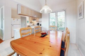 A dining area with a wooden table and chairs, a hanging light fixture, and a view through a window with blinds. - Stewards Watch ownhouse close to the ccean w/shared pool, free WiFi, private W/D (Bethany Beach)