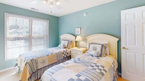 A bedroom with two beds, a ceiling fan, a window with blinds, and a door.
