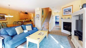 A living room with a blue sofa, a coffee table, a fireplace, and a staircase leading to another room.