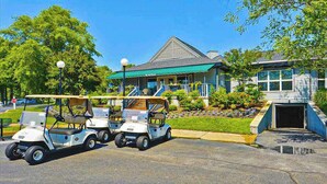 A building with a green awning, a covered porch, and a parking area with golf carts.